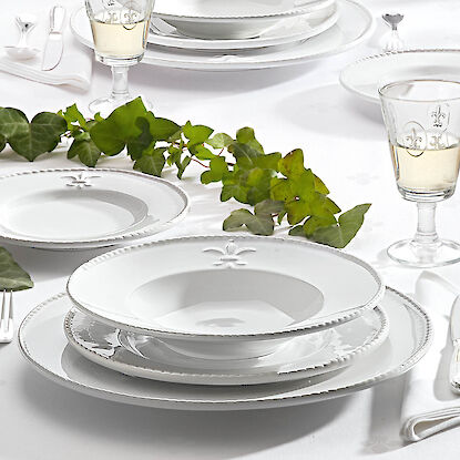 Service de table blanc élégant avec motif fleur de lys, verres à vin et décoration de lierre.