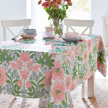 „Nappe fleurie avec vaisselle et bouquet dans une salle à manger lumineuse.