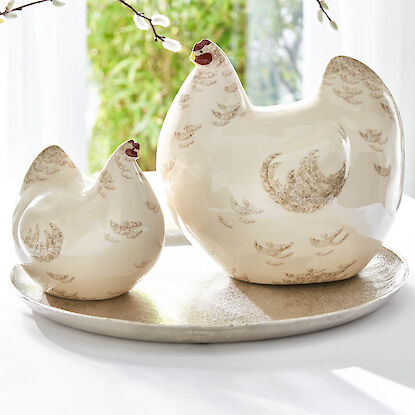 Poules en céramique sur plateau avec branches printanières.