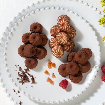 Feine Schokoladen- und Karamell-Pralinen in Gugelhupf-Form auf edlem Teller mit Himbeeren