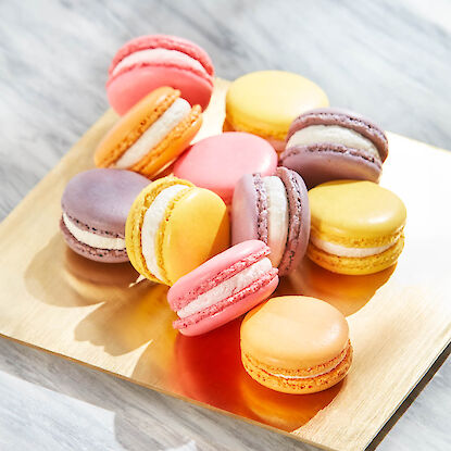 Macarons français colorés avec une garniture crémeuse sur un plateau doré élégant.