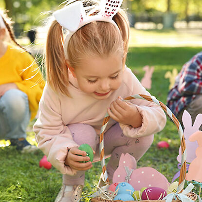 Enfant avec des oreilles de lapin cherchant des œufs de Pâques et remplissant un panier