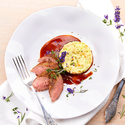 Magret de canard rosé avec sauce à la lavande et risotto aux légumes, servi sur une assiette élégante