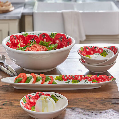 Tomaten-Dekor Geschirr mit Caprese-Salat und Burrata auf Holztisch in heller Küche.