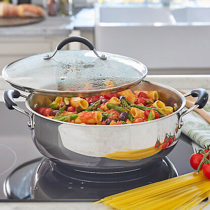 Pâtes aux tomates et asperges vertes dans une casserole en inox sur plaque à induction.