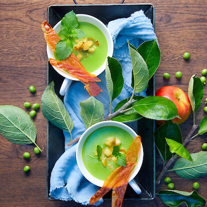 Soupe de pois avec pommes, bacon croustillant et menthe, servie en tasses sur un plateau