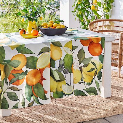 Tisch mit Zitronen-Orangen-Tischläufer auf Terrasse, dekoriert mit Zitrusfrüchten und Korbstuhl