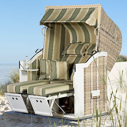 Strandkorb mit grün-beiger Polsterung in den Dünen am Meer, bei blauem Himmel