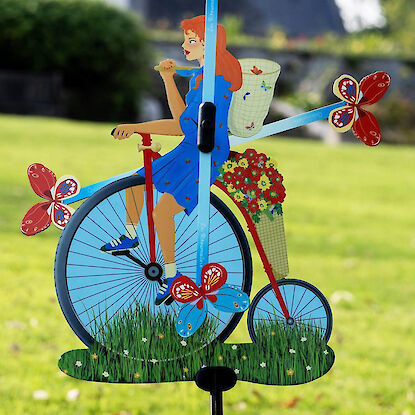 Bunte Garten-Windmühle in Fahrradform mit Frau, Blumen und Schmetterlingen auf grüner Wiese