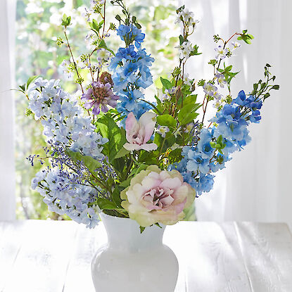 Bunter Frühlingsblumenstrauß mit blauen und rosafarbenen Blüten in weißer Vase