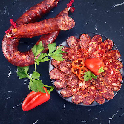 Chorizo cru entier et en tranches, accompagné de poivron, persil et du label de qualité Gourmetfleisch.