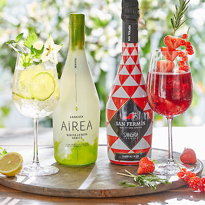 Zwei Sangria-Flaschen mit passenden Cocktails, garniert mit Zitrone, Beeren und Kräutern auf Tablett.