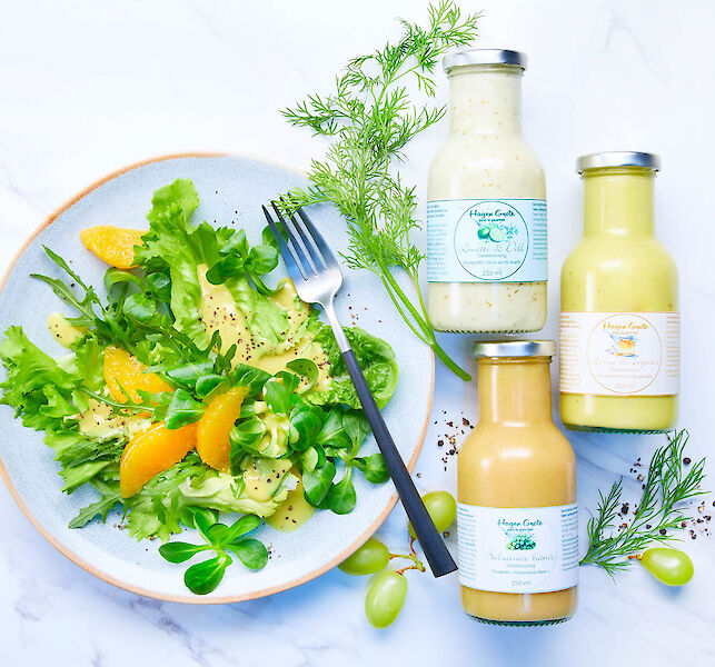 Frischer Salat mit Orangenfilets, daneben drei Premium-Dressings in Flaschen und frische Kräuter.