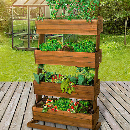 Vertikales Hochbeet aus Holz mit Kräutern, Salat und Gemüse auf Terrasse, im Hintergrund ein Gewächshaus.