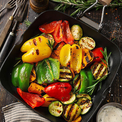 Gegrilltes Gemüse in Grillpfanne mit Paprika, Zucchini, Süßkartoffeln und Rosmarin, serviert mit Dip.