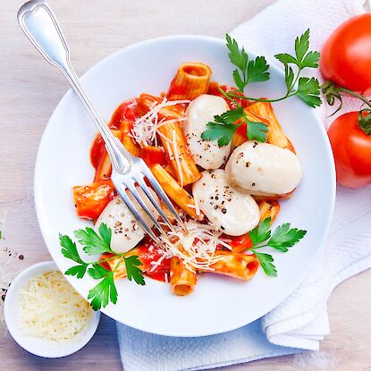 Pasta mit Tomatensauce, Mozzarella, Petersilie und Parmesan, serviert auf einem weißen Teller.