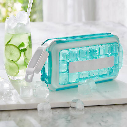 Eiswürfelform mit Deckel und Drink mit Limettenscheiben und Eiswürfeln auf Marmorplatte.