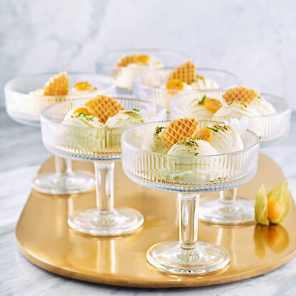 Eis-Desserts in eleganten Glas-Schalen mit Waffeln, Physalis und Deko auf goldfarbenem Tablett.