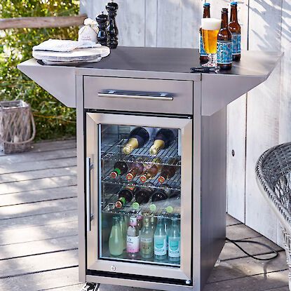 Mobiler Getränkekühlschrank mit Glastür, gefüllt mit Flaschen, auf Terrasse neben Bier und Snacks.