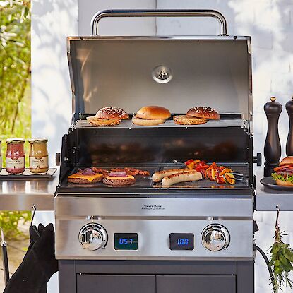 Gasgrill mit Burgern, Würstchen, Gemüse und Saucen, umgeben von Kräutern, Bier und Gewürzen.