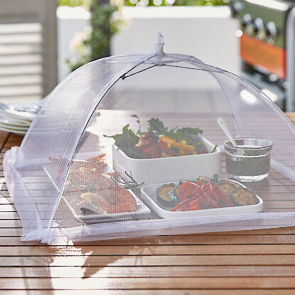 Schalen mit gegrilltem Gemüse und Garnelen unter einem feinmaschigen Abdecknetz auf Holztisch.