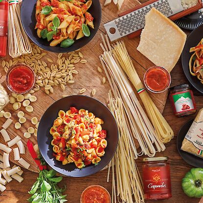 Italienische Pasta, Tomatensaucen, Parmesan und frische Kräuter auf Holztisch mit roten Servietten.