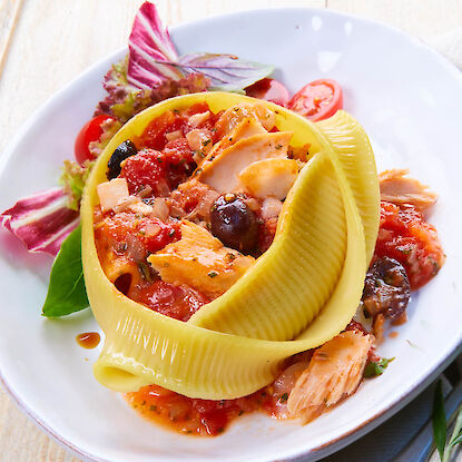 Gefüllte Riesenmuschel-Nudel mit Tomatensauce, Thunfisch, Oliven und Salatgarnitur auf weißem Teller.