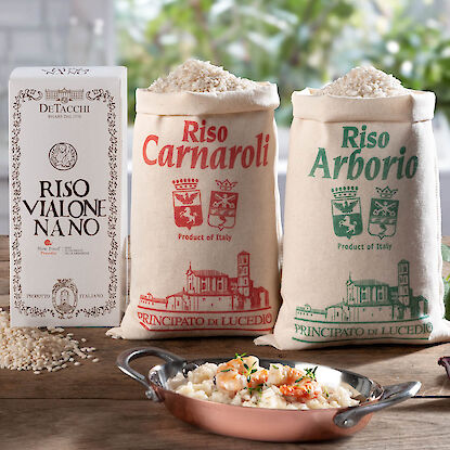 Drei Sorten italienischer Risottoreis in Verpackungen mit Schale cremigem Risotto auf Holztisch.