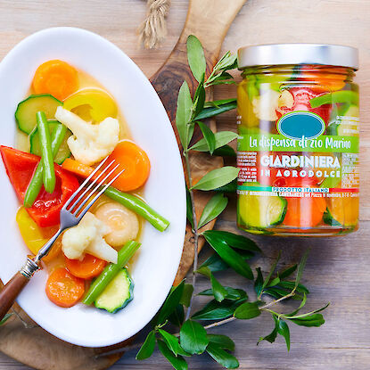 Bunte eingelegte Gemüse auf weißem Teller mit Gabel, daneben Glas italienische Giardiniera.