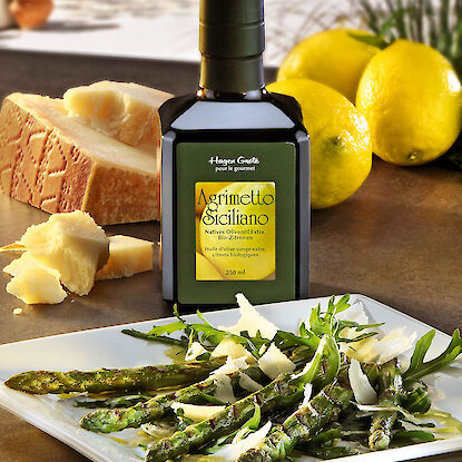 Grüner Spargel mit Rucola und Parmesan auf Teller, dazu Zitronen-Olivenöl und Käsestück im Hintergrund.
