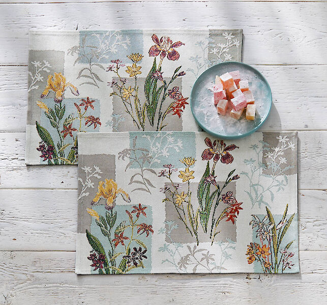 Blumen-Tischsets mit türkisem Teller und Würfeln aus Lokum auf weißem Holztisch.