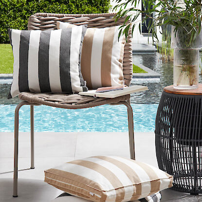Gestreifte Outdoor-Kissen auf Stuhl und Boden neben Pool, mit Buch und Pflanzen-Deko.