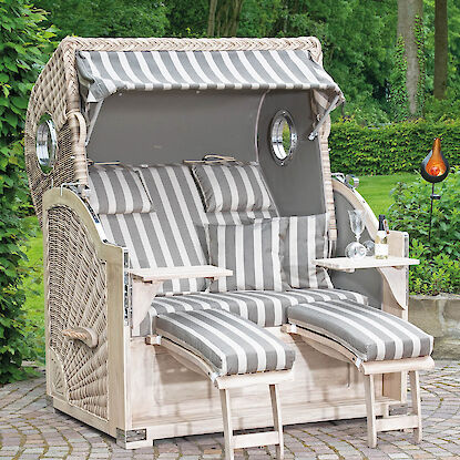 Großer Strandkorb mit grauen Streifenpolstern, Fußstützen und Ablage auf Terrasse im Garten.