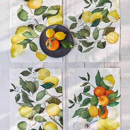 Vier Tischsets mit Zitronen- und Orangenmotiven, dekoriert mit schwarzem Teller und Obst.