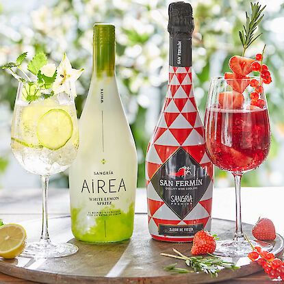 Zwei Sangriaflaschen mit dekorierten Gläsern, Zitrone, Beeren und Kräutern auf Holzteller.