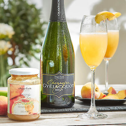 Champagnerflasche, Bellini-Püree und Pfirsichcocktails mit Fruchtgarnitur auf Holztisch.