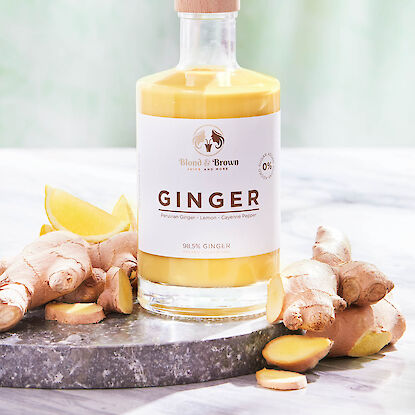 Ingwer-Shot-Flasche mit Zitronenstücken und frischem Ingwer auf Marmorteller.