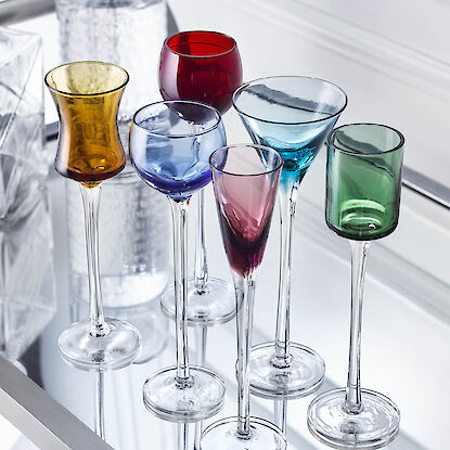 Sieben bunte Cocktail- und Likörgläser aus Glas auf silbernem Tablett.