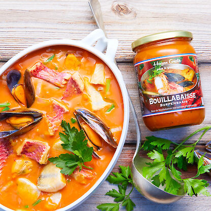 Bouillabaisse mit Muscheln, Fisch und Gemüse in Schale, daneben Suppenbasis im Glas.