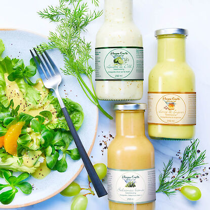 Drei Flaschen Salatdressing neben grünem Blattsalat mit Orange, Kräutern und Trauben.