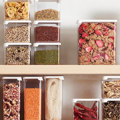 Vorratsgläser mit Trockenprodukten wie Linsen, Müsli, Nudeln und Gewürzen im Regal.
