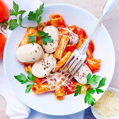 Pasta mit Tomatensauce, Mozzarella, Parmesan und Petersilie auf weißem Teller.