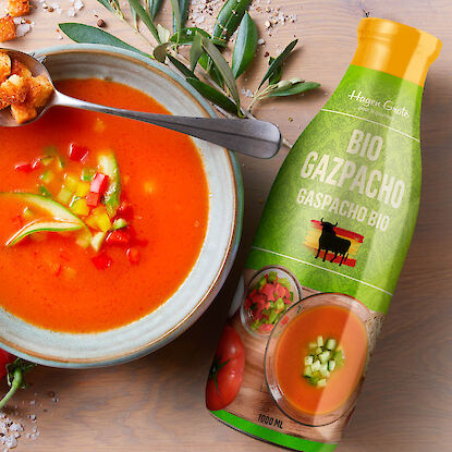 Flasche Bio-Gazpacho neben Schüssel kalter Gemüsesuppe mit Croutons.