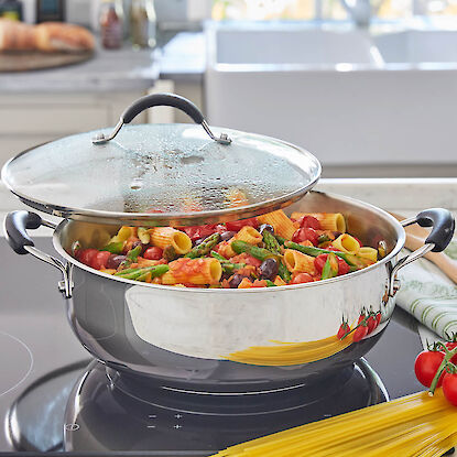 Edelstahlpfanne mit Pasta, grünem Spargel und Tomaten auf einem Induktionskochfeld.