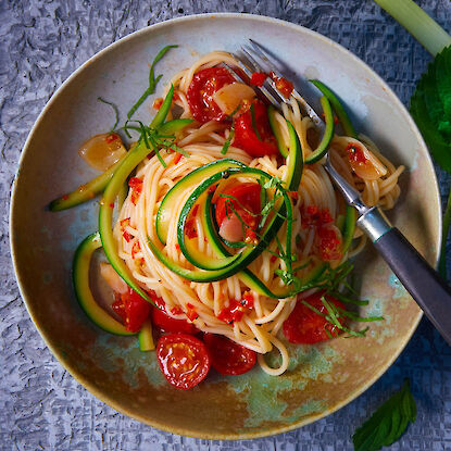 Spaghetti mit Zucchinistreifen, Kirschtomaten und Kräutern auf Keramikteller angerichtet.