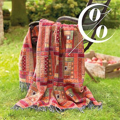 Bunte Decke auf Gartenstuhl, daneben Apfelkiste im Gras und ein Prozentzeichen als Angebotshinweis.