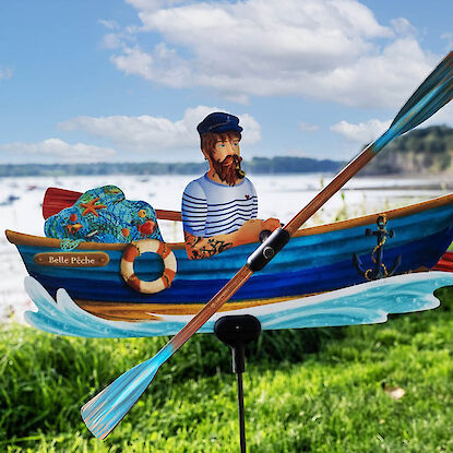 Bunte Windfigur mit Seemann im Ruderboot vor See und Wiese, Dekoration für den Garten.
