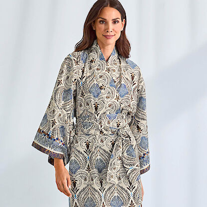 Frau trägt gemusterten Kimono mit blau-beigem Blätterdesign vor hellem Hintergrund.
