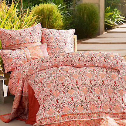 Bettwäsche in warmen Orange-Rot-Tönen mit orientalischem Muster auf Terrasse im Grünen.
