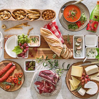 Table méditerranéenne avec pain, fromages, saucissons, jambon, gaspacho, crackers, raisins, figues et dips.